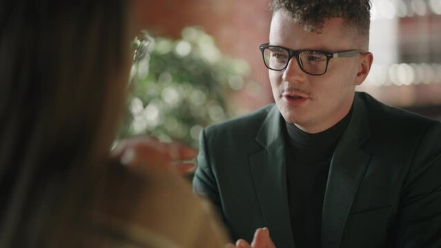 Man with glasses conducts negotiations talks and conducts a job interview or discusses issues with a woman sitting at a table. Business meeting of a man and a woman, a dialogue between two partners