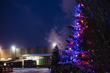 Christmas tree in a snowy city at night. Smoke from the chimney of a large enterprise envelops the snowy city. The concept of a warm winter in Ukraine and Europe.