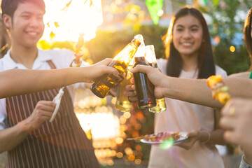 A group of Asian friends clinks a wine bottle during a party barbecue.