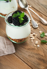 Yogurt with granola, blackberry berry fruits and muesli served in glass jar on wooden background....
