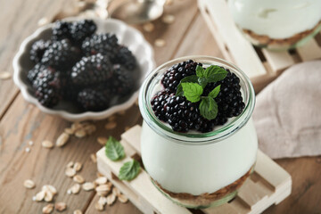 Yogurt with granola, blackberry berry fruits and muesli served in glass jar on wooden background. Healthy breakfast concept. Healthy food for breakfast, top view