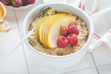 Oatmeal. Bowl of oatmeal porridge with raspberry, pear and honey on gray concrete old table background. Hot and healthy food for Breakfast, top view, flat lay