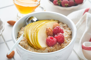 Oatmeal. Bowl of oatmeal porridge with raspberry, pear and honey on gray concrete old table background. Hot and healthy food for Breakfast, top view, flat lay