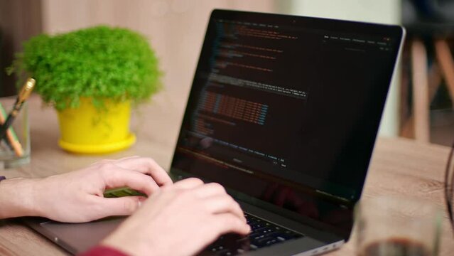 Close up of freelancer's hands typing code on laptop keyboard. Camera slides around developer's figers writing program code on computer display. Programmer working on online application database.