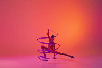 Studio shot of young charming girl, rhythmic gymnast training with sports equipment isolated over...