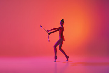 Fototapeta na wymiar Studio shot of young charming girl, rhythmic gymnast training with sports equipment isolated over pink background in neon light filter