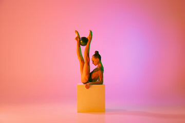 Studio shot of young charming girl, rhythmic gymnast training with sports equipment isolated over...