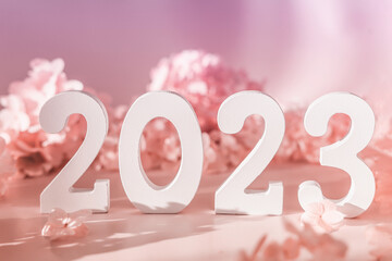 White wooden number 2023 on pastel pink background with flowers. Top view, flat lay. Happy New Year...