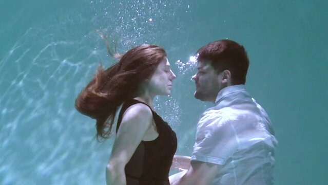 A woman and a guy are swimming underwater. A woman kisses a guy underwater.
