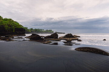 Volcanic sandy beach with ocean and waves in Balian. Beach with rocks and cloudy sky