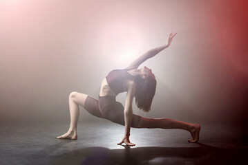 Flexible young female woman doing exercise in fog/ smoke. Girl wearing fitness dance clothing...