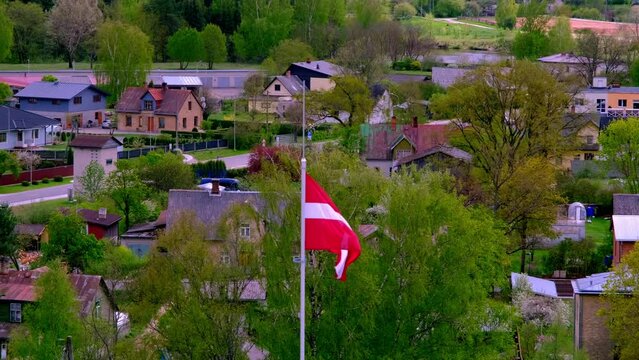 Valmiera, Latvia - 17 May 2022: the national Latvian flag flutters in the wind with Valmiera City in the background from an aerial view.