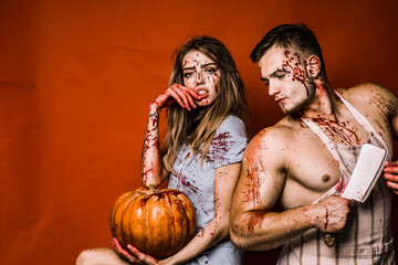 Crazy Halloween couple on red background isolated. Couple in blood. Animal hunger. Strong man wearing butcher apron with blood stains. Happy Halloween.