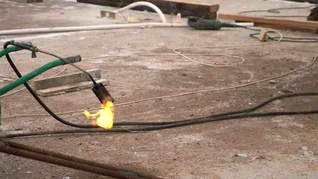 A hose with a burning gas burner on a construction site on the sand. Burning blowtorch for melting. Orange flames roll out of a torch after finished waterproofing process.