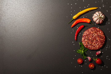 Raw steak cutlets from minced beef meat on black stone background. Fresh vegetables, mint