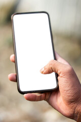 One hand holds a mobile phone and its screen is white and the background blur