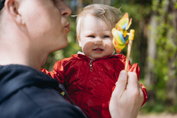 father holding baby daughter blowing plastic hand windmill