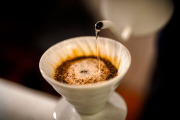 Barista making a Geisha coffee, pouring hot water from kettle over a ground coffee powder