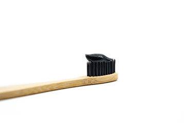 Whitening black charcoal toothpaste on bamboo toothbrush, close up. Eco natural product for dental...