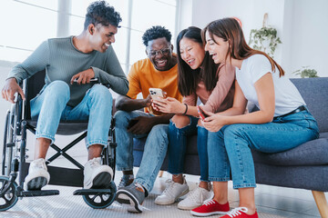 Man on wheelchair with friends having fun watching smart mobile phone device - Happy teenagers...