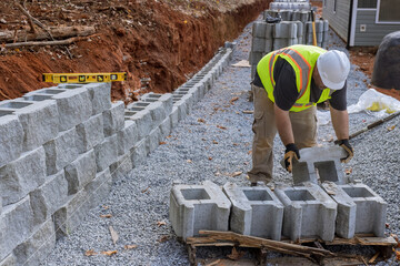 Construction site worker installing newly constructed large block retaining wall construction near...