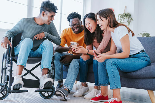 Man on wheelchair with friends having fun watching smart mobile phone device - Happy teenagers posting picture on social media - Youth lifestyle concept