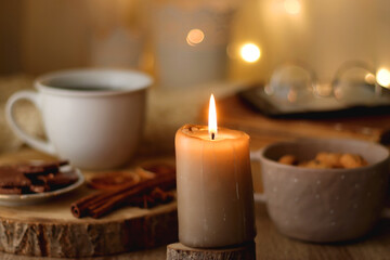 Fototapeta na wymiar Bowl of cookies, cup of tea or coffee, chocolate, spices, knitted blanket, books, glasses and candle on the table. Cozy hygge atmosphere at home. Selective focus.