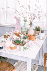 happy easter and spring holidays time. festive tablescape set decor. traditional dinner food easter eggs and baked cakes on table at home. rabbit and willow. pale pop pastel blue and pink color