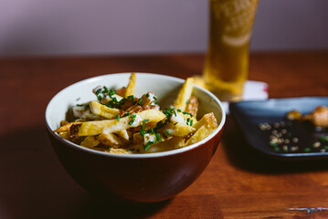 bowl of gourmet fried chips inside a restaurant with soft light and beer in background. fancy side dish or appetizer with sauce and chives and Parmesan Truffle