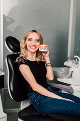 A woman in a dentist's chair holds a jaw with braces in her hands