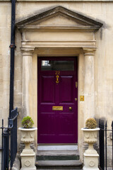 Fototapeta na wymiar Entrance with purple wooden door and fence at famous City of Bath on a cloudy summer day. Photo taken August 2nd, 2022, Bath, United Kingdom.