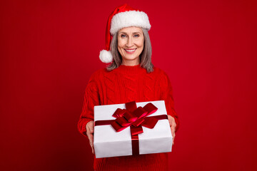 Photo of dreamy cheerful granny hold present package toothy smile wear hat pullover isolated red color background