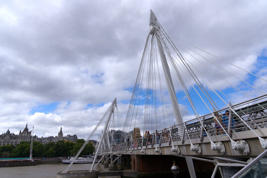 Hungerford railway bridge and Golden Jubilee Bridges with pedestrians crossing at City of Westminster on a cloudy summer day. Photo taken August 3rd, 2022, London, United Kingdom.