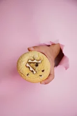 Tuinposter Hand holding chocolate bar cookie on the pink background, vertical © Nina Ljusic/Wirestock Creators