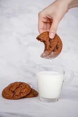 Fotobehang Chocolate cookie soaked in a cup of milk for breakfast, vertical © Nina Ljusic/Wirestock Creators
