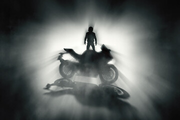 Silhouette of a motorcycle rider with a helmet and defocused race motorcycle with fog