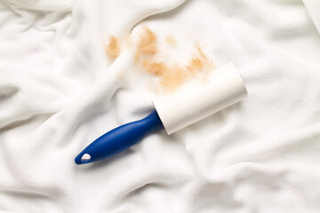 Cloth cleaner lint roller brush with paper roll blue grip on white color fabrics background. sticky roller, pet cat dog fur dust hair remover. Top view. Flat lay