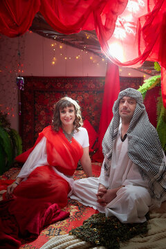 Portrait of young arabian muslim couple in traditional clothes in cozy red room. Fhoto shoot in easten style with male and female model like in a harem with a sultan and an odalisque