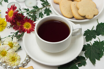 A cup of tea on a table with flowers on a white background. Tea and biscuits for breakfast
