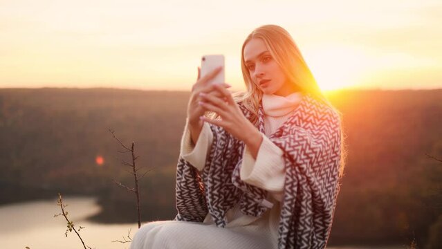 Happy blond young woman using smart phone in the mountains. Attractive young woman posing, takes selfies and streams video to social media from her smartphone.