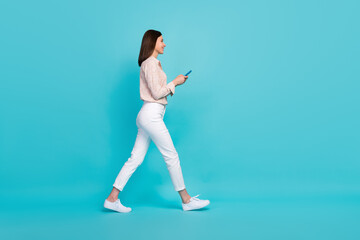 Fototapeta na wymiar Full size photo of pretty young girl walking hold device chatting dressed stylish smart casual look isolated on aquamarine color background