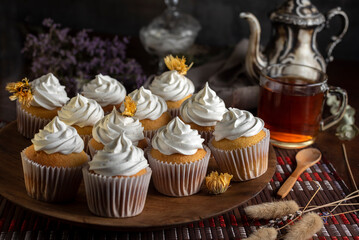 muffins or madeleines on a can and a wooden board with meringue and cream on top with an old teapot cup of tea and decorated with natural flowers