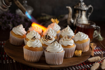 muffins or madeleines on a can and a wooden board with meringue and cream on top with an old teapot cup of tea and decorated with natural flowers