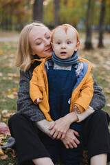 Happy caucasian woman with little baby boy. Mother and son walking and having fun together among autumn leaves. Parent playing with toddler outdoors. Family, parenthood, childhood, happiness concept.