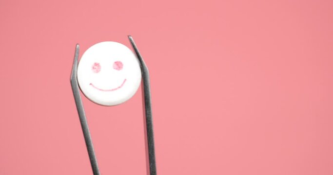happy smile pill in tweezers close up, lsd tablet for good psychoactive trip on pink background. High quality 4k footage