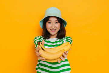 Asian young woman wearing panama smiling while holding bananas