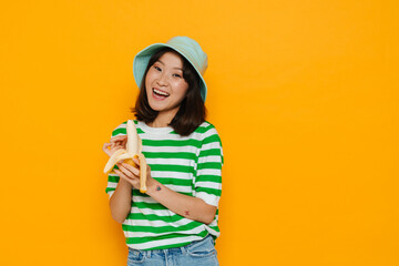 Asian young woman wearing panama smiling while eating banana
