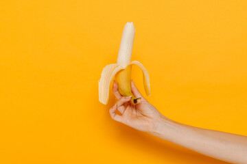 Fototapeta na wymiar Young white female hand holding banana isolated over yellow wall