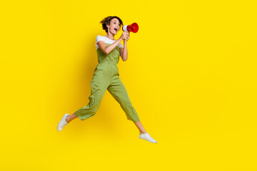 Fototapeta na wymiar Full length photo of young attractive screaming girl wear khaki overalls hold loudspeaker strike against low salary isolated on yellow color background