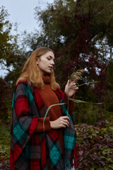 a beautiful woman in a plaid poncho walks in the forest enjoying nature and relaxation, holding a branch of reeds in her hand